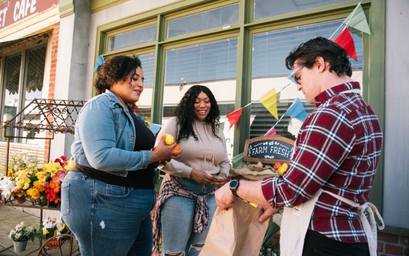 Image from gallery: Three individuals with obesity converse together outside at a farmer's market